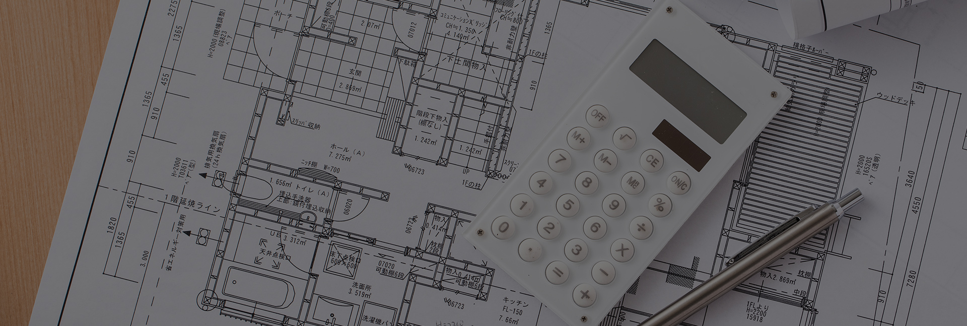写真：設計図の上に置かれたペンと電卓